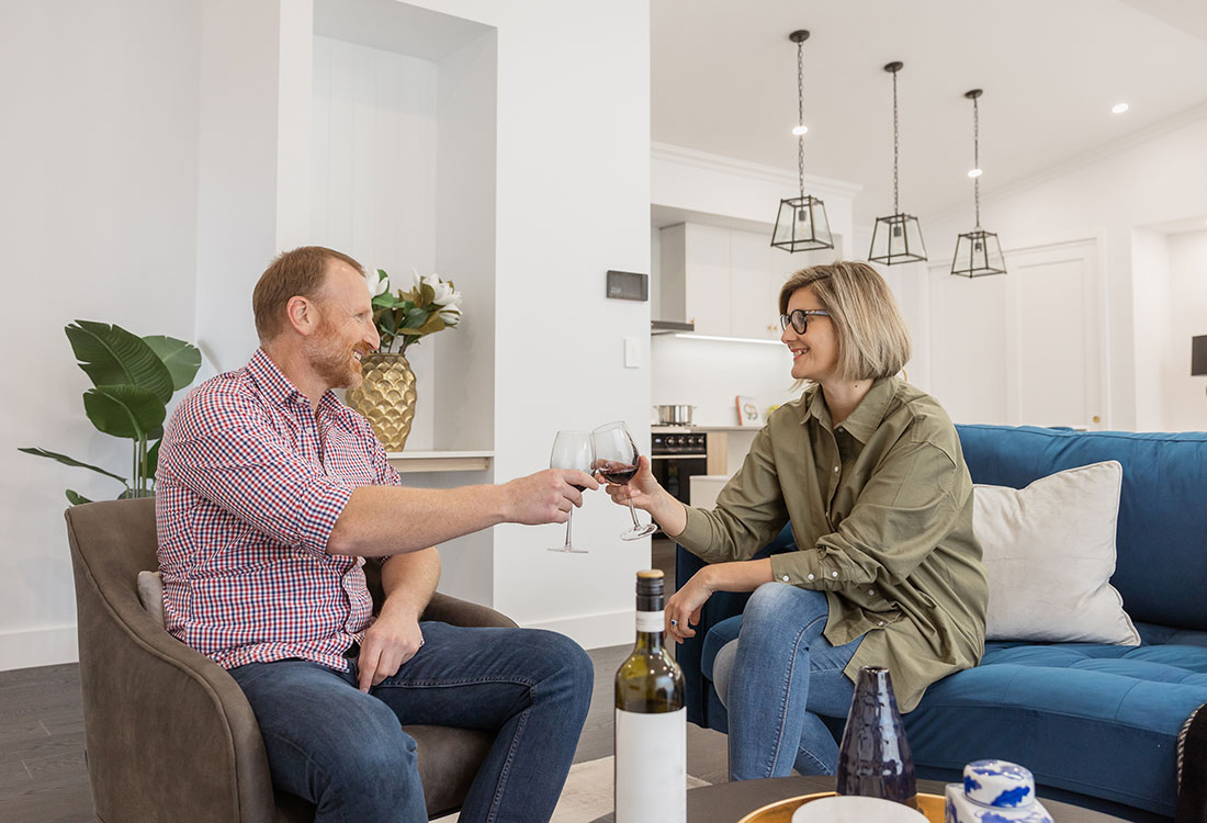Couple sitting on lounges in a Maas home, clinking wine glasses