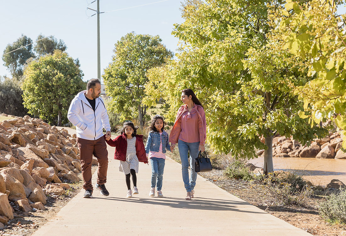 Family walking holding hands along a path in leafy Southlakes, Dubbo